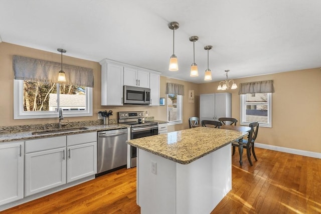 kitchen with white cabinetry, sink, decorative light fixtures, a kitchen island, and appliances with stainless steel finishes