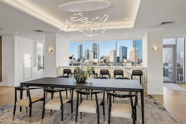 dining room featuring a tray ceiling, a wall of windows, a chandelier, and light parquet flooring