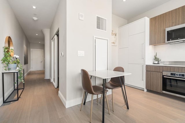 kitchen featuring white cabinetry, stainless steel appliances, a kitchen bar, and light wood-type flooring