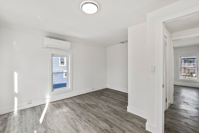 unfurnished room with a wall mounted air conditioner, a wealth of natural light, and dark hardwood / wood-style floors