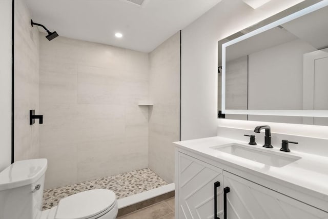 bathroom featuring tile patterned flooring, vanity, a tile shower, and toilet