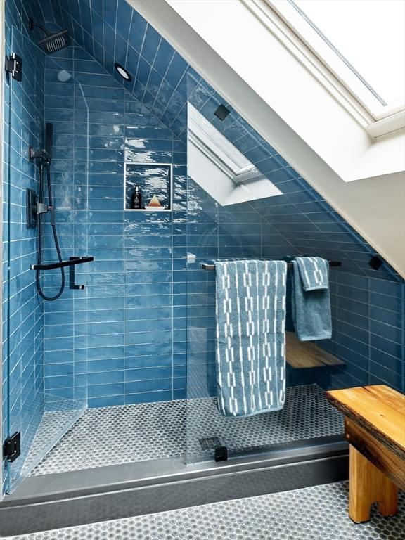 bathroom with a stall shower, a skylight, and tile walls