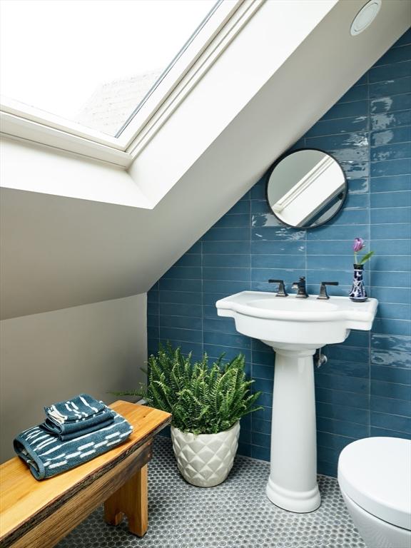 half bath featuring a skylight, tile walls, vaulted ceiling, and toilet