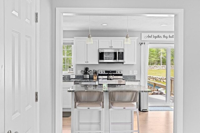 111 Spruce St, Middleboro, MA 02346 - kitchen with stainless steel appliances, white cabinets, light wood-type flooring, a breakfast bar area, and dark stone countertops