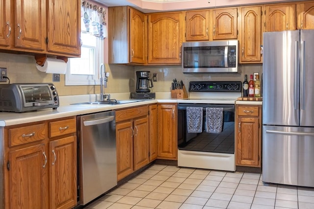 kitchen with light tile patterned flooring, stainless steel appliances, a sink, light countertops, and brown cabinetry