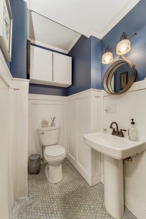 bathroom with crown molding, toilet, wainscoting, and a decorative wall
