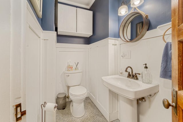 half bath with tile patterned flooring, a wainscoted wall, toilet, ornamental molding, and a decorative wall