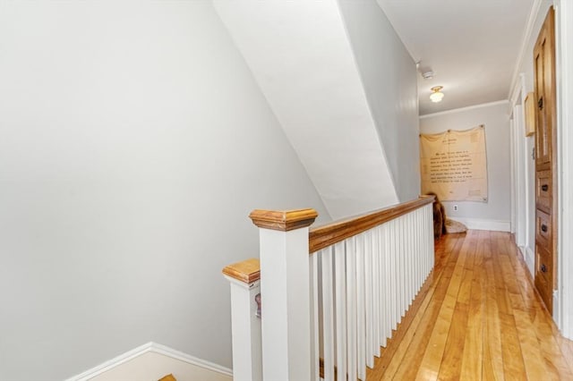 hallway with light wood-style floors, baseboards, crown molding, and an upstairs landing
