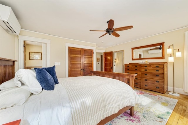 bedroom with a closet, light wood-style floors, baseboards, ceiling fan, and a wall unit AC