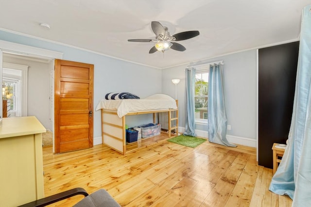 bedroom featuring baseboards, ornamental molding, a ceiling fan, and light wood-style flooring