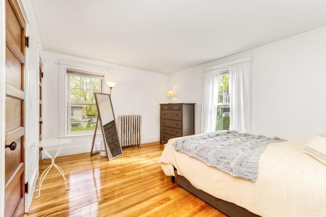 bedroom featuring baseboards, multiple windows, radiator heating unit, and light wood-style flooring