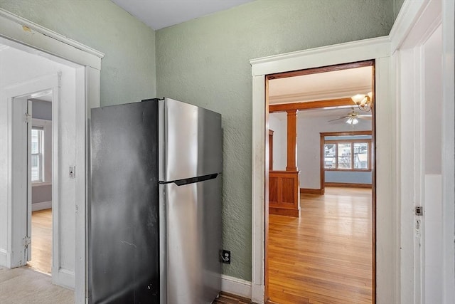 kitchen with a textured wall, light wood-style flooring, freestanding refrigerator, ceiling fan, and baseboards