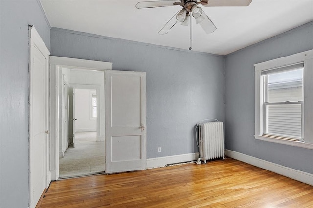 spare room with baseboards, ceiling fan, light wood finished floors, and radiator