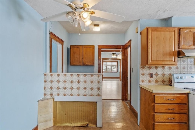 kitchen featuring white electric stove, decorative backsplash, light countertops, a textured ceiling, and under cabinet range hood