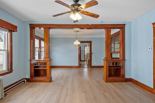 empty room with a baseboard heating unit, light wood-style flooring, baseboards, and ornate columns