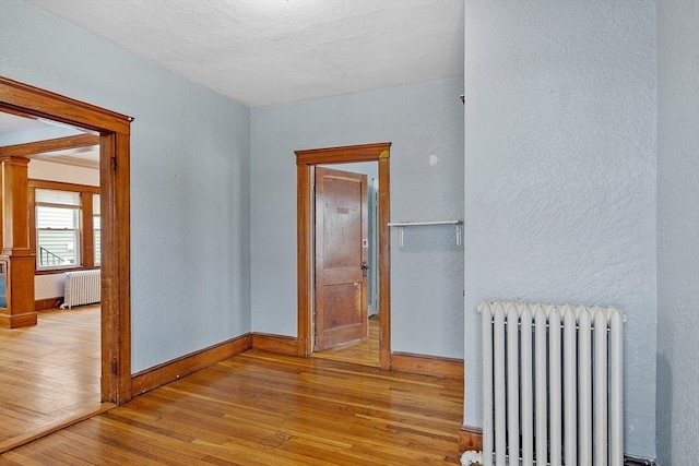 spare room with radiator, light wood finished floors, decorative columns, and baseboards