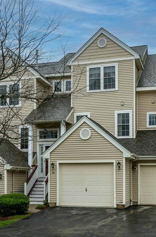 townhome / multi-family property with a garage, aphalt driveway, and roof with shingles