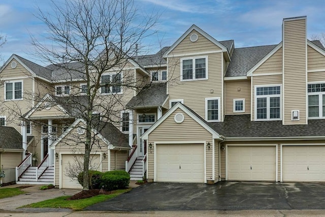 multi unit property featuring a chimney, stairs, roof with shingles, and aphalt driveway