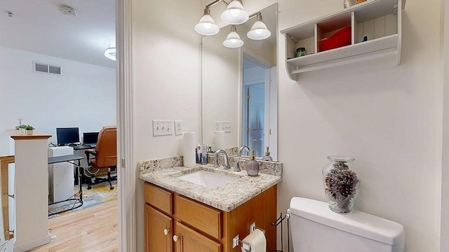 half bathroom featuring vanity, visible vents, toilet, and wood finished floors