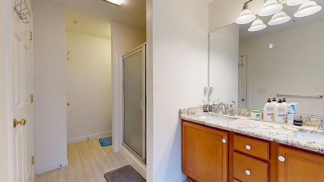 full bathroom with a shower stall, double vanity, a sink, and baseboards