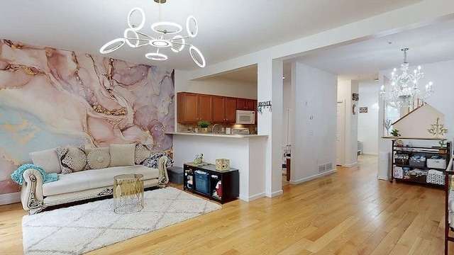 living room featuring visible vents, baseboards, light wood finished floors, and an inviting chandelier