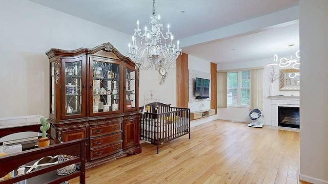 bedroom featuring baseboards, an inviting chandelier, light wood-style floors, and a fireplace with flush hearth