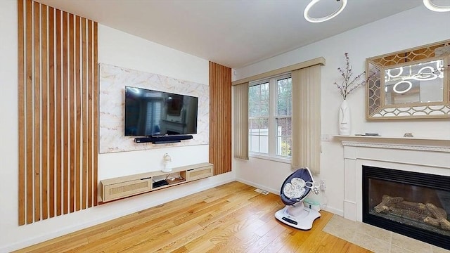 unfurnished living room featuring a glass covered fireplace, visible vents, baseboards, and wood finished floors