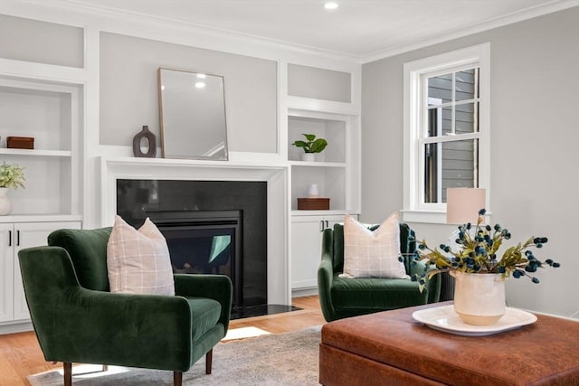 sitting room featuring built in shelves, crown molding, and light hardwood / wood-style flooring