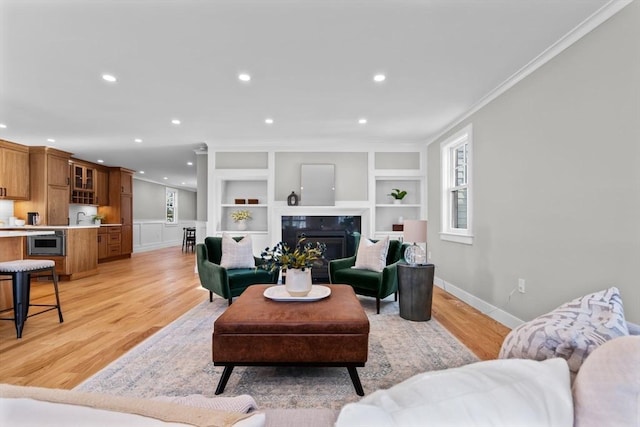 living room featuring ornamental molding, built in features, a high end fireplace, and light hardwood / wood-style flooring