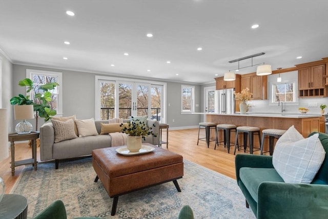 living room featuring sink, crown molding, french doors, and light wood-type flooring