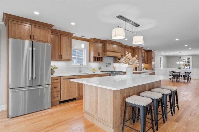 kitchen with sink, light wood-type flooring, stainless steel fridge, dishwasher, and a large island