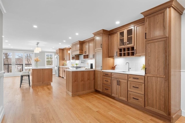 kitchen featuring sink, high end fridge, ornamental molding, light hardwood / wood-style floors, and a kitchen bar