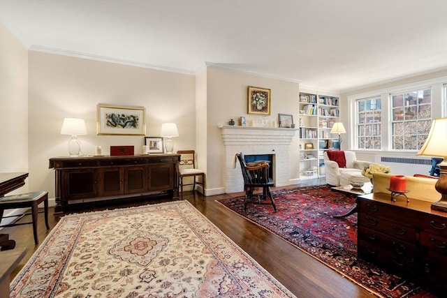 living room featuring radiator, built in shelves, dark wood-type flooring, a brick fireplace, and crown molding