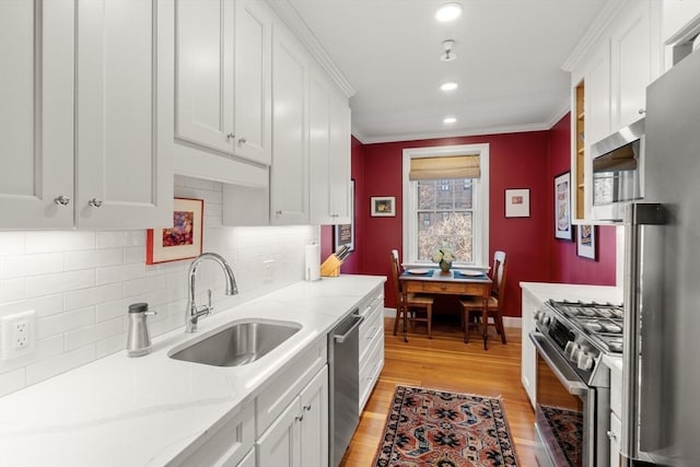 kitchen with sink, light stone countertops, light wood-type flooring, appliances with stainless steel finishes, and white cabinetry