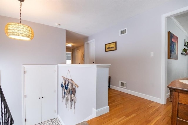 corridor with light wood-style flooring, an upstairs landing, visible vents, and baseboards