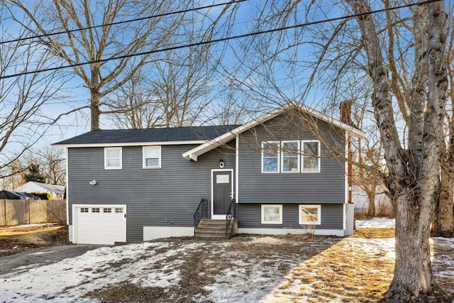 bi-level home featuring entry steps, aphalt driveway, a garage, fence, and a chimney