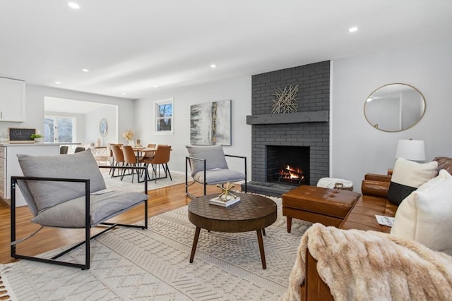 living area featuring recessed lighting, a brick fireplace, baseboards, and light wood finished floors