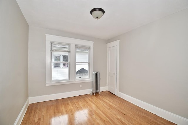 unfurnished room featuring radiator, baseboards, and light wood-type flooring