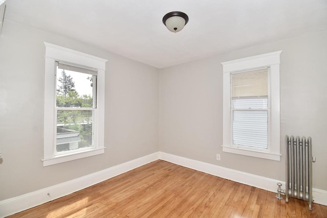 unfurnished room with radiator heating unit, light wood-type flooring, and baseboards