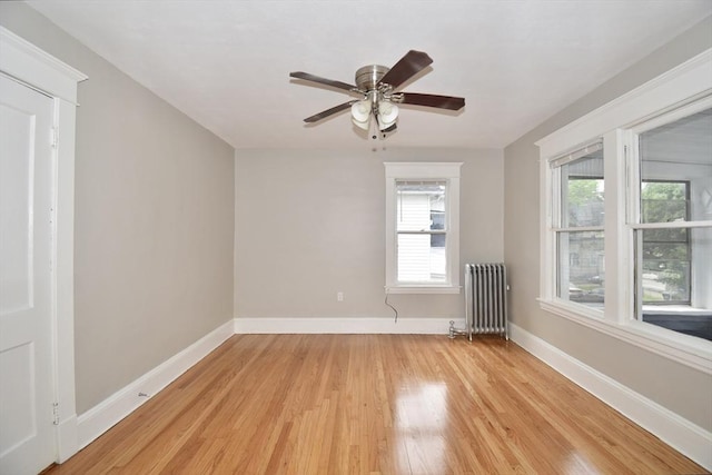 empty room featuring radiator heating unit, light wood-style floors, healthy amount of natural light, and baseboards