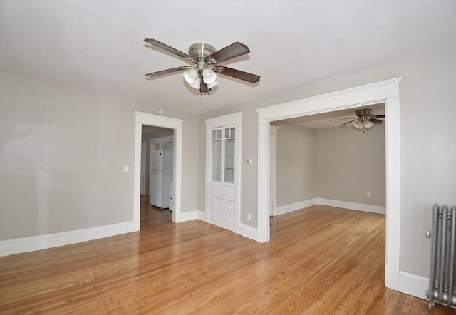 empty room with radiator heating unit, ceiling fan, light wood finished floors, and baseboards