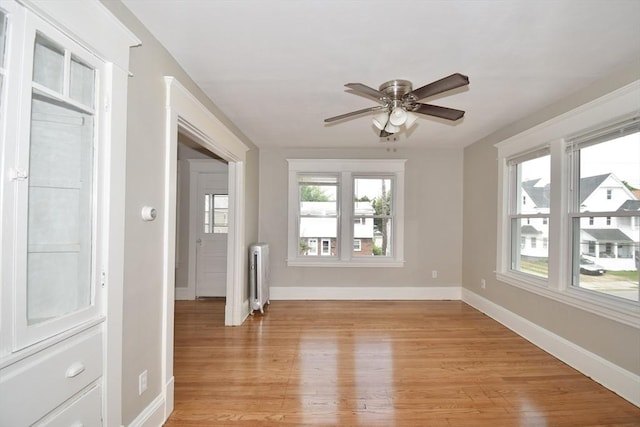 empty room featuring radiator, baseboards, ceiling fan, and light wood-style flooring