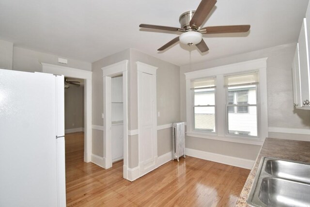 kitchen featuring freestanding refrigerator, radiator, ceiling fan, light wood finished floors, and baseboards