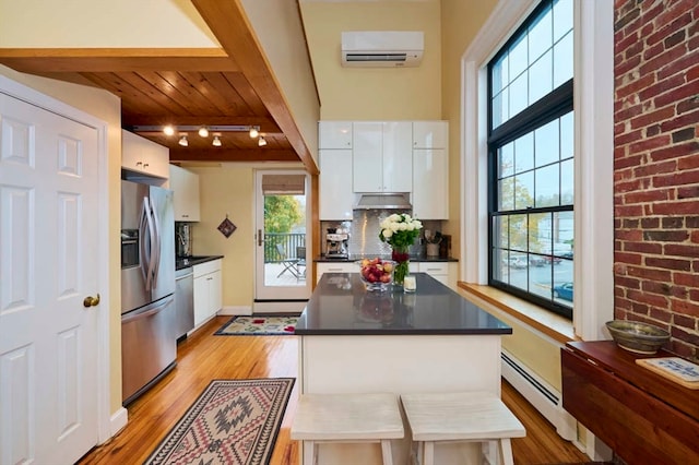 kitchen with white cabinetry, appliances with stainless steel finishes, a wall mounted AC, rail lighting, and light hardwood / wood-style flooring