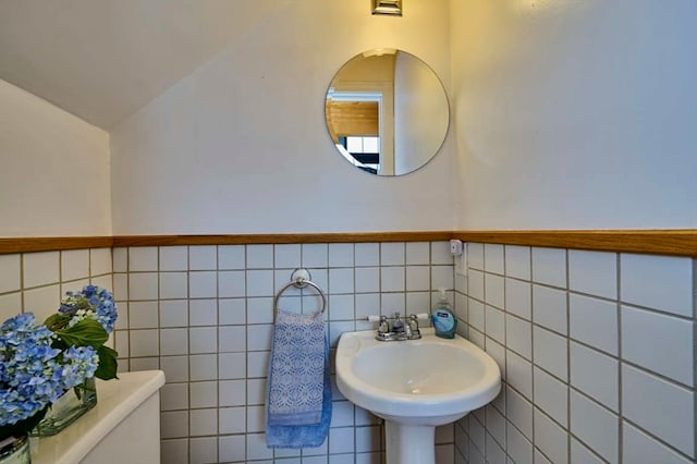 bathroom with tile walls, lofted ceiling, sink, and toilet