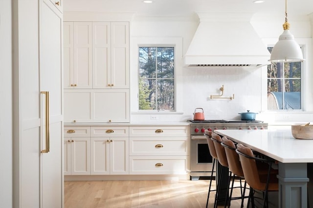 kitchen featuring light countertops, white cabinets, premium range hood, and high end stainless steel range oven