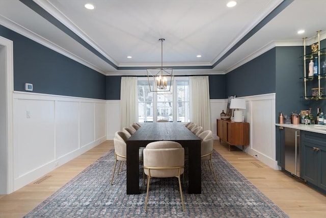 dining area with light wood-type flooring, a wainscoted wall, a tray ceiling, and crown molding