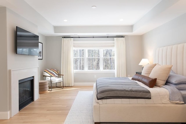 bedroom featuring light wood-type flooring, a glass covered fireplace, baseboards, and recessed lighting