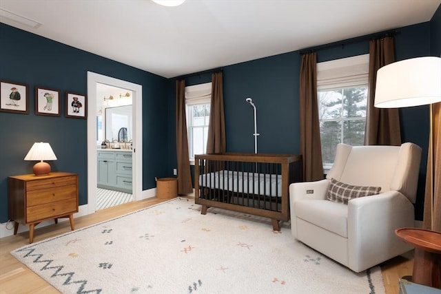 bedroom featuring baseboards, multiple windows, wood finished floors, and connected bathroom