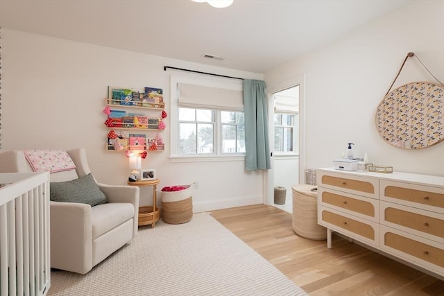 bedroom featuring light wood-style floors, baseboards, visible vents, and a nursery area